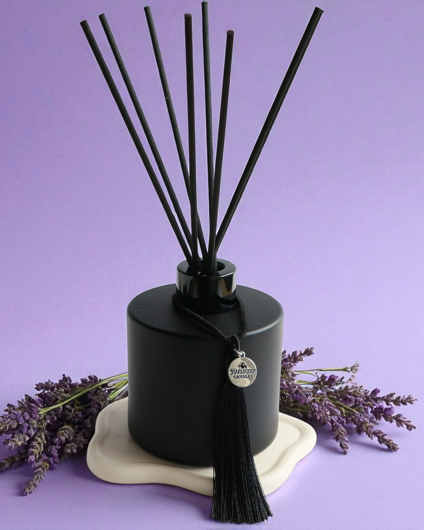 An Australian made Harlequin Candles black matte reed diffuser with a calming and relaxing fragrance of lavender and vanilla, set against a purple background with lavender sprigs.