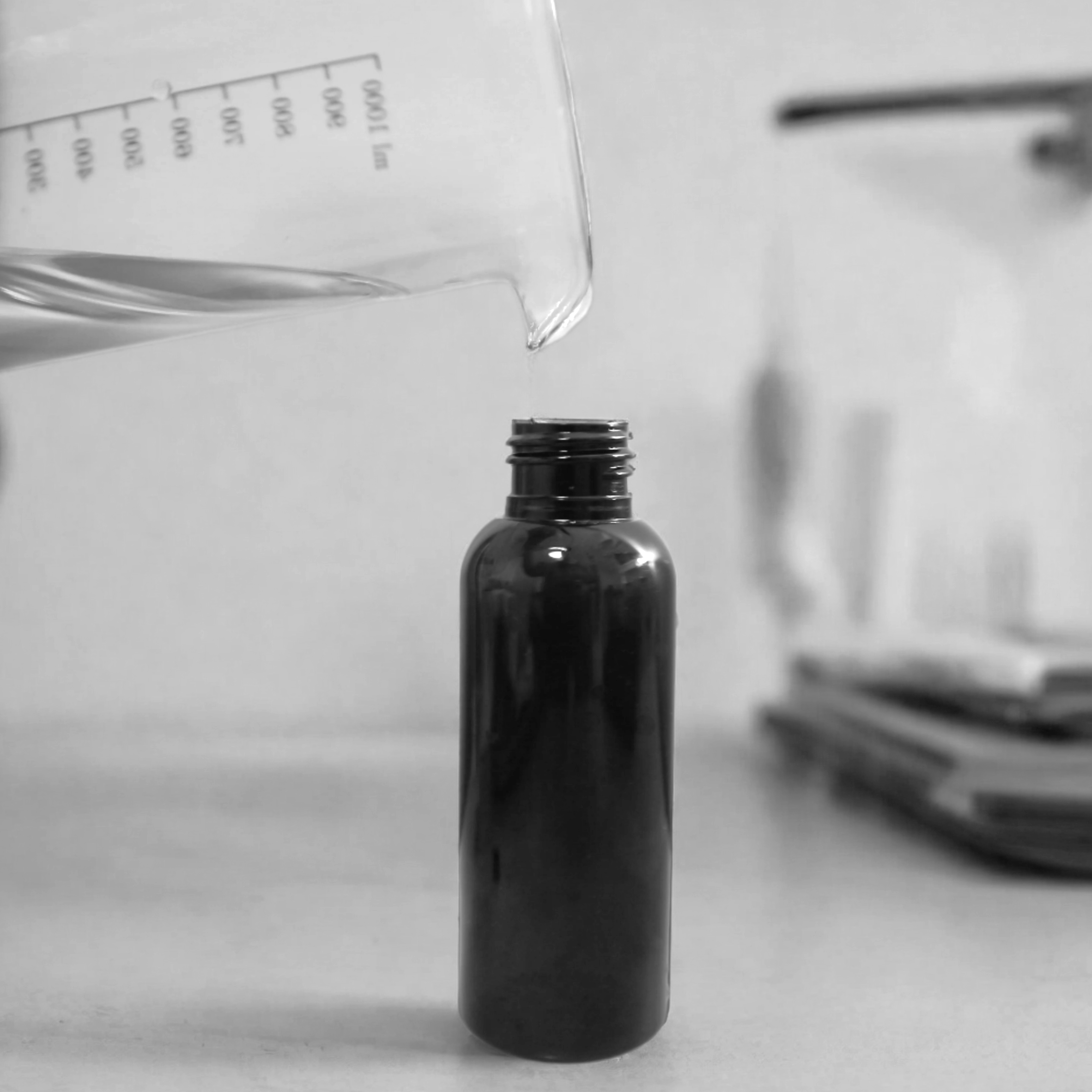 Behind the scenes at Harlequin Candles: Close-up of liquid being carefully poured from a beaker into a small brown bottle with a black pump, illustrating the craftsmanship of making our signature room mists.