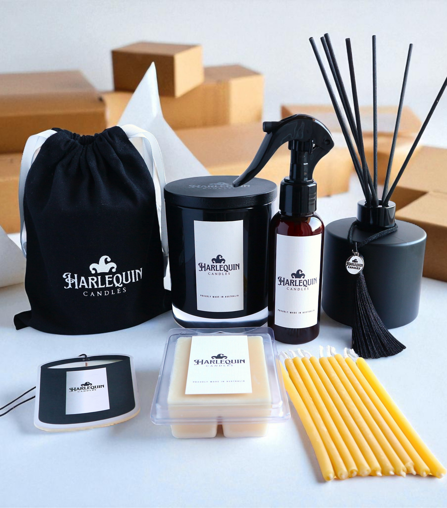 Open Harlequin Candles gift box showcasing a variety of home fragrance items nestled in brown shredded paper. Includes a black jar candle, soy wax melts in a clear clamshell, a room mist spray, and a branded black drawstring bag. 'Thank You For Your Order' is printed on the inside of the box lid. Promotes customizable Australian-made gift sets.