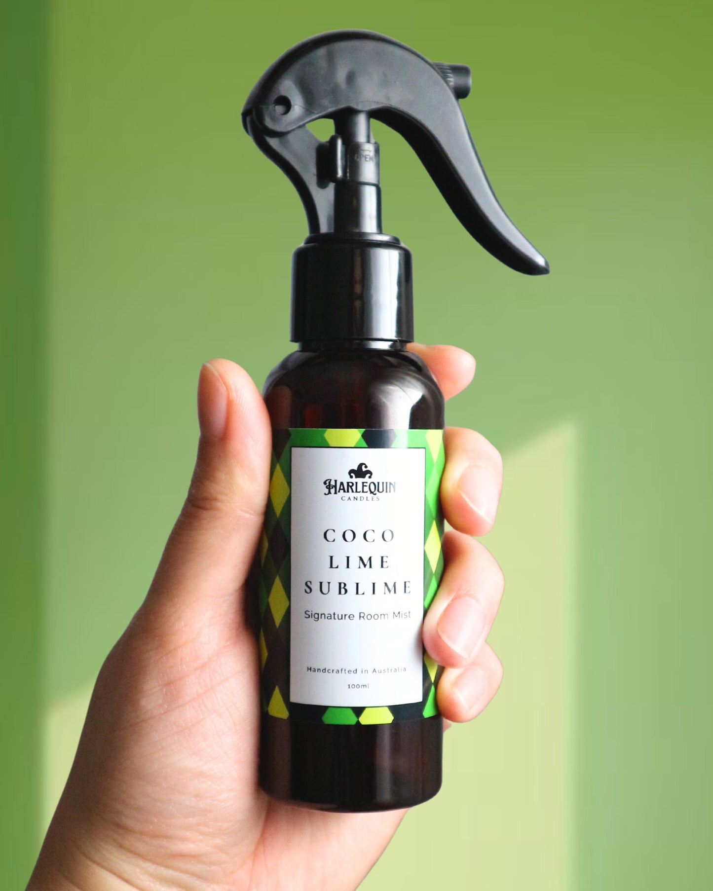 A Harlequin Candles Coco Lime Sublime Signature Room Mist in an amber spray bottle with a black trigger cap, placed against a two-toned background of light green and white. The label clearly shows 'Harlequin Candles', 'Coco Lime Sublime', 'Signature Room Mist', and 'Handcrafted in Australia', highlighting this tropical Australian-made home spray.