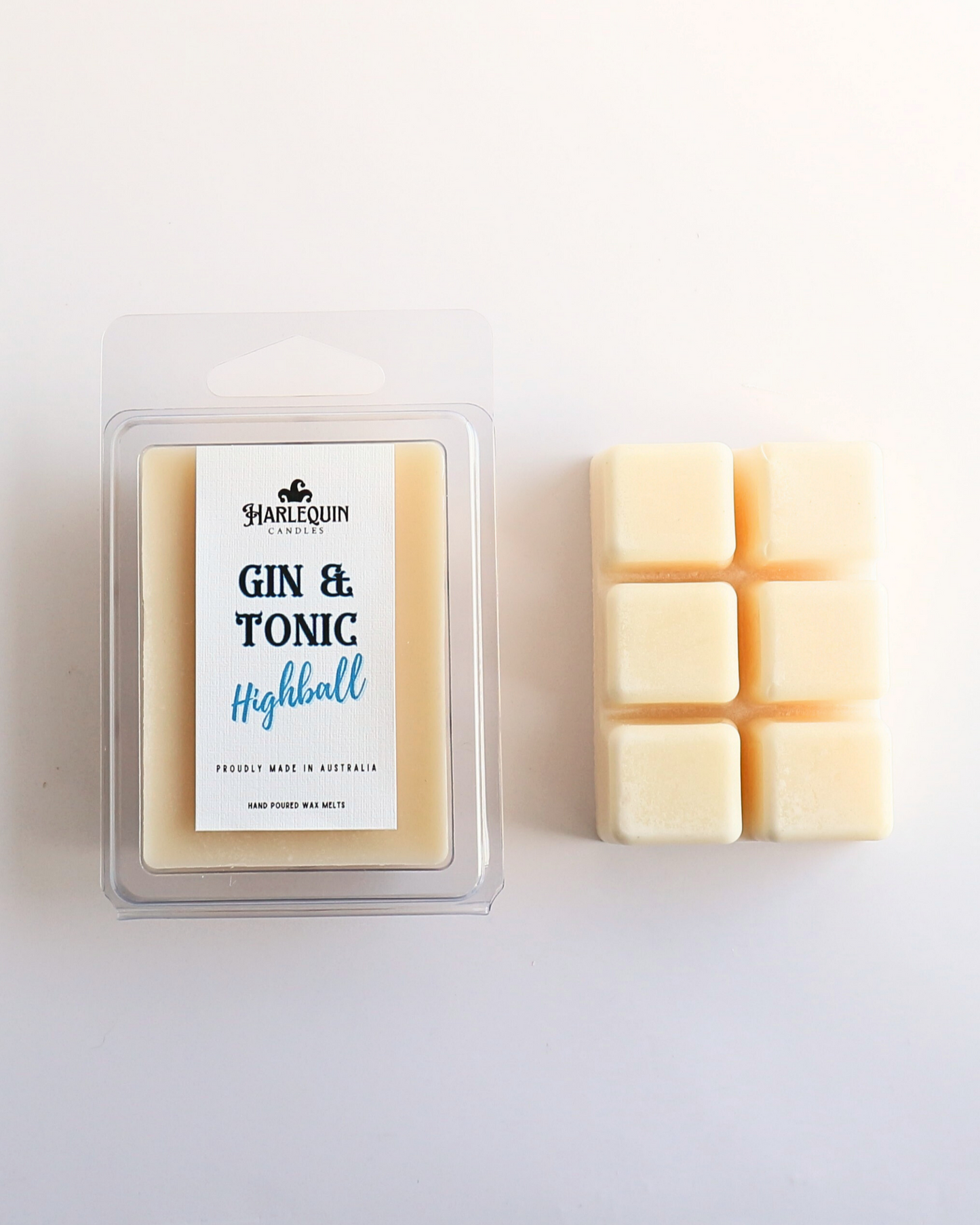 Harlequin Candles Gin & Tonic Highball soy wax melts, displayed in clear plastic clamshell packaging with the brand label. The label reads 'GIN & TONIC Highball' and 'PROUDLY MADE IN AUSTRALIA HAND POURED WAX MELTS'. Several individual wax melt cubes are scattered on a light wooden cutting board, showcasing the refreshing home fragrance product and its local origin.