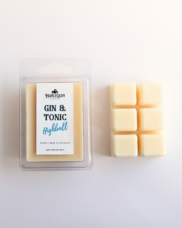 Harlequin Candles Gin & Tonic Highball soy wax melts, displayed in clear plastic clamshell packaging with the brand label. The label reads 'GIN & TONIC Highball' and 'PROUDLY MADE IN AUSTRALIA HAND POURED WAX MELTS'. Several individual wax melt cubes are scattered on a light wooden cutting board, showcasing the refreshing home fragrance product and its local origin.