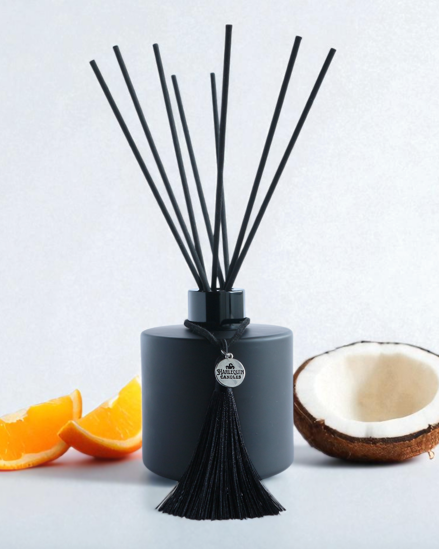 Harlequin Candles Tropical Tush reed diffuser in a matte black bottle with black reeds and a decorative black tassel. Scented like popular Brazilian bum bum creams, ideal for a summery home fragrance.