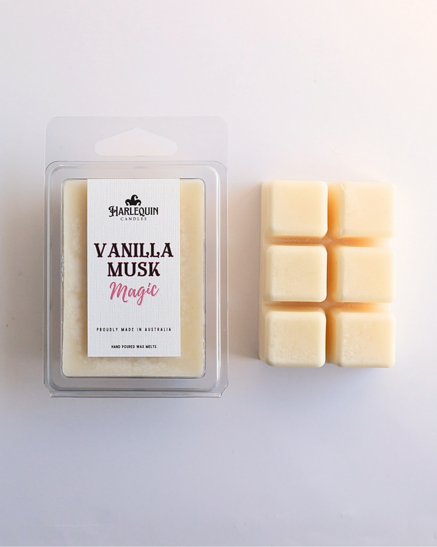 Harlequin Candles Vanilla Musk Magic soy wax melts, displayed in clear plastic clamshell packaging with the brand label visible. The label reads 'VANILLA MUSK Magic' and 'PROUDLY MADE IN AUSTRALIA HAND POURED WAX MELTS'. Several individual wax melt cubes are scattered on a light wooden cutting board, showcasing the product and its local origin.