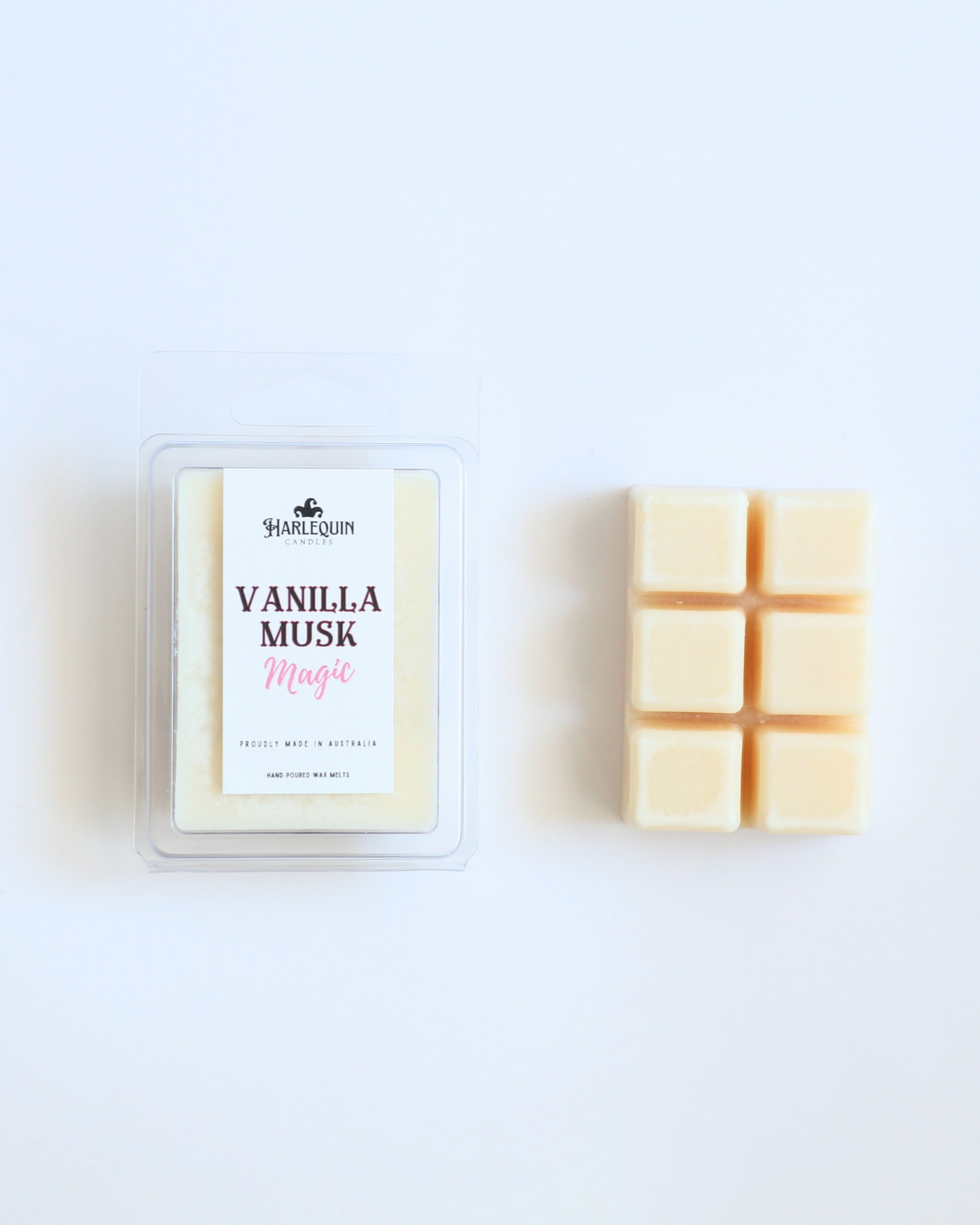 Harlequin Candles Vanilla Musk Magic soy wax melts, displayed in clear plastic clamshell packaging with the brand label visible. The label reads 'VANILLA MUSK Magic' and 'PROUDLY MADE IN AUSTRALIA HAND POURED WAX MELTS'. Several individual wax melt cubes are scattered on a light wooden cutting board, showcasing the product and its local origin.
