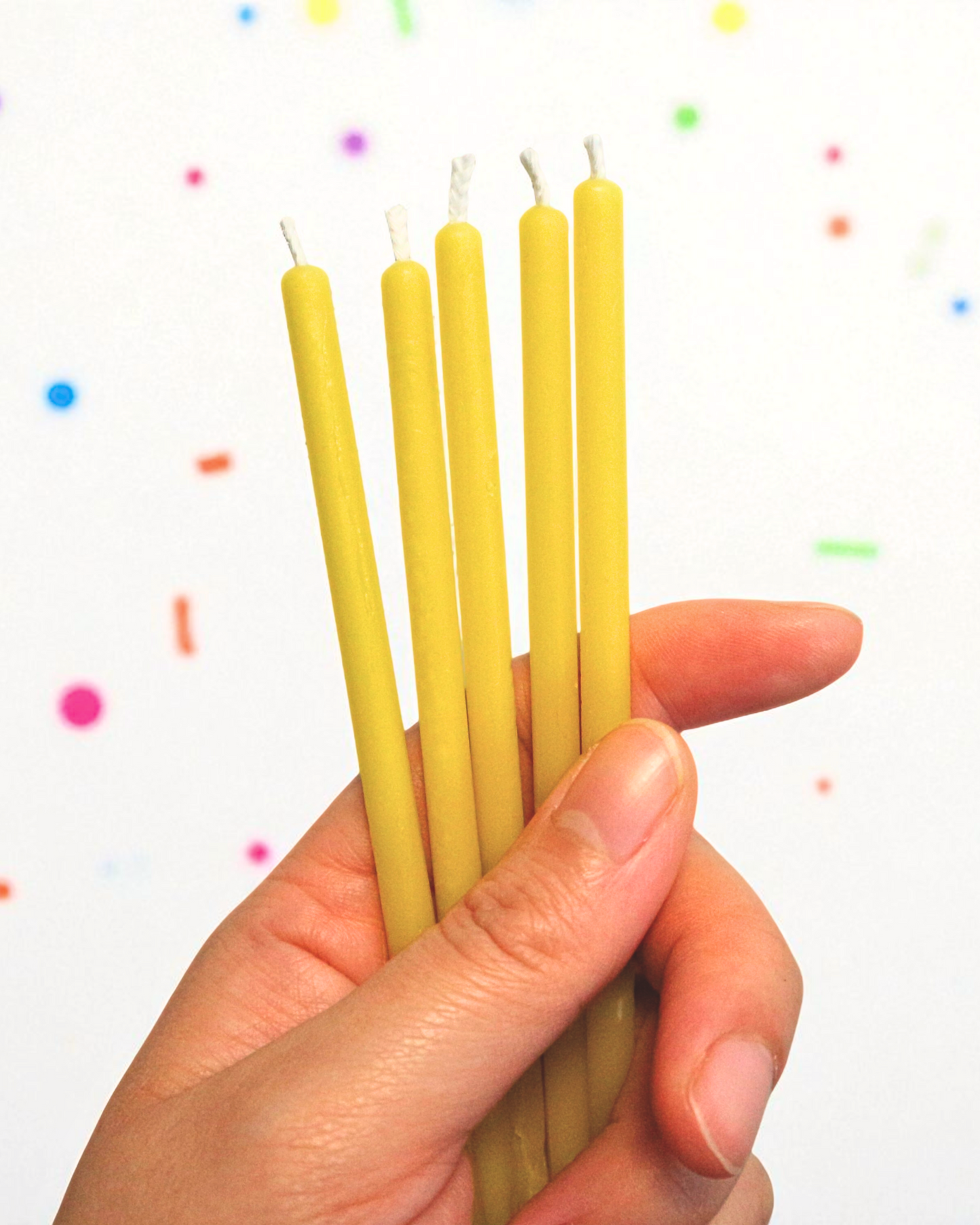 Hand holding five yellow candles against a plain background