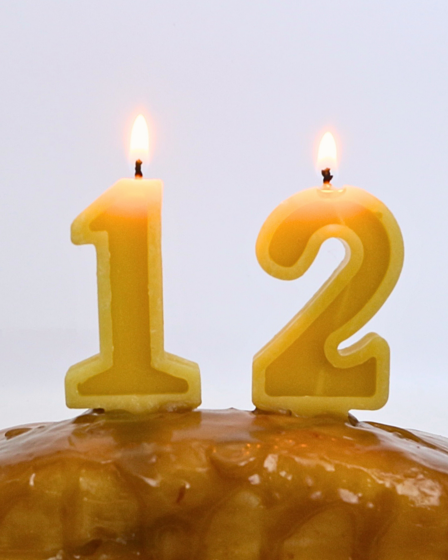 Two yellow number candles on a cake against a light gray background