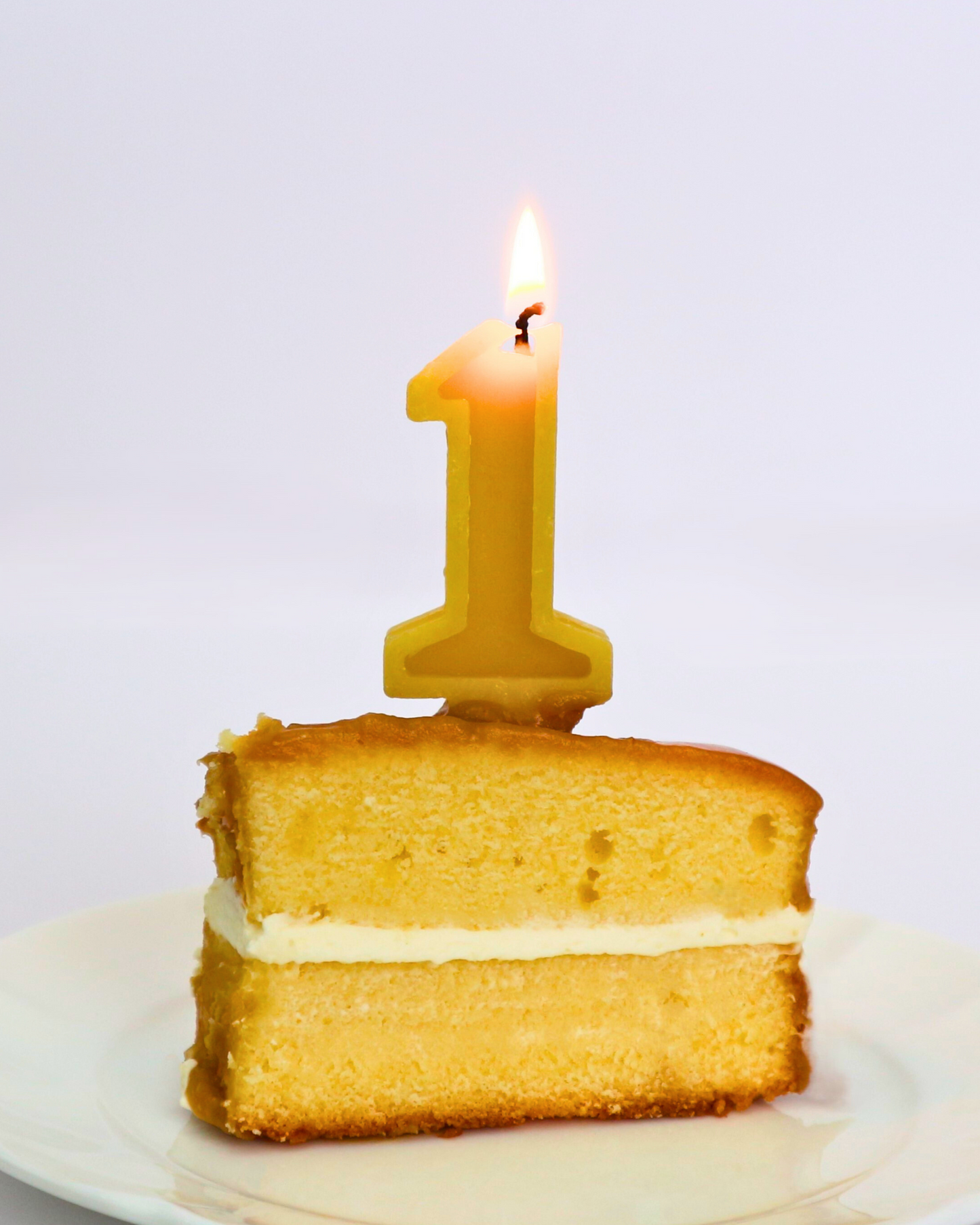 Slice of birthday cake with a lit number '1' candle on a white background