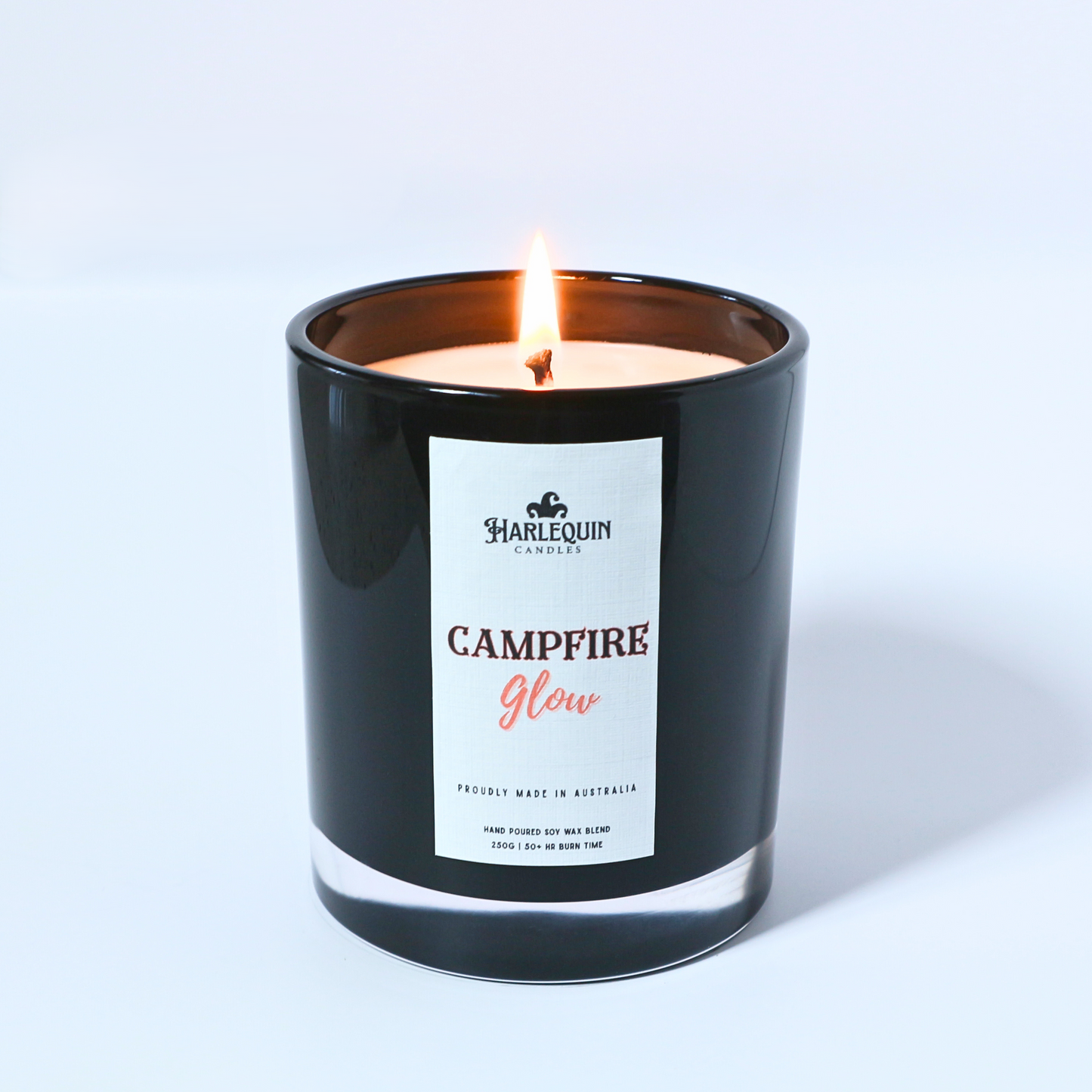 Harlequin Candles 'Campfire Glow' scented candle in a black jar with a white label, proudly made in Australia. Hand-poured soy wax blend, 250g, 50+ hour burn time, with a rich campfire smoke scent.