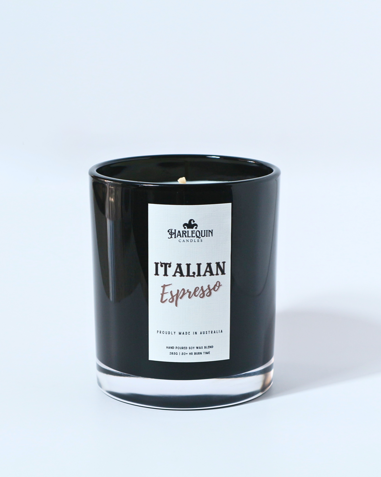 A Harlequin Candles "Italian Espresso" hand-poured soy wax candle in a black glass jar, resting on a blue book. Premium Australian made scented candle.