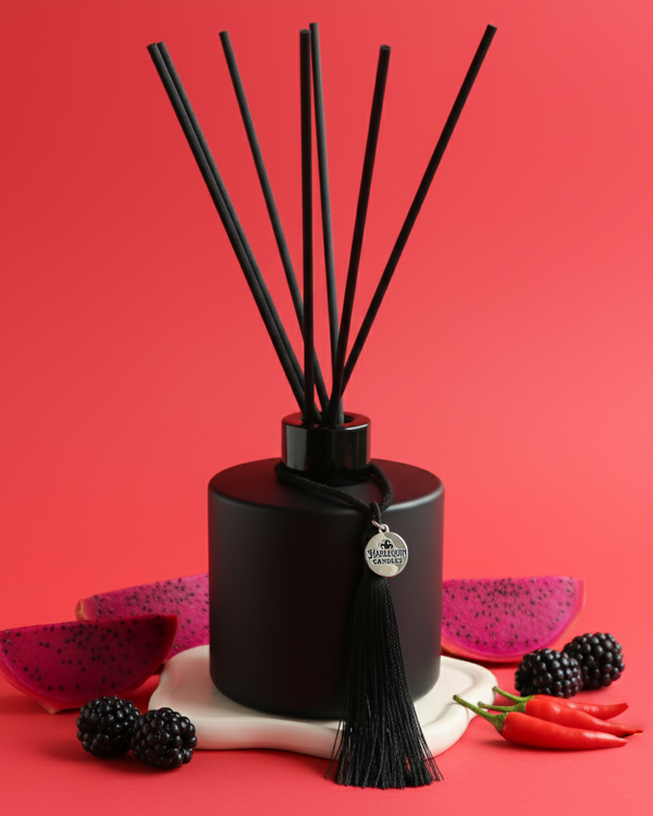 An Australian made Harlequin Candles reed diffuser with an exotic and spicy home scent called Fruit & Fire.The product is shown on a red background with dragonfruit, blackberries, and chili peppers and chipotle.