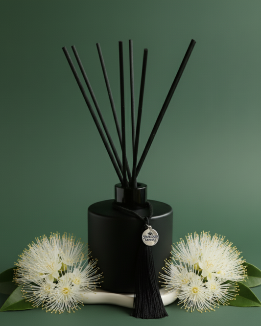 An Australian made Harlequin Candles reed diffuser with a fresh floral home fragrance of orange blossom and lemon myrtle, set against a vibrant green background with Australian Lemon Myrtle blossoms and green leaves.