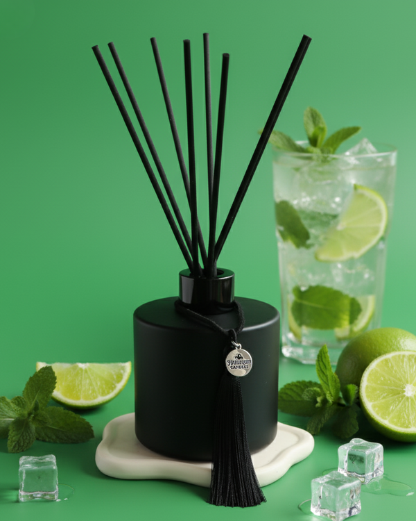 An Australian made Harlequin Candles black matte reed diffuser with a zesty scent inspired by a mint mojito cocktail. The product is on a green background with limes, spearmint leaves, and ice cubes.