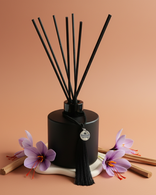 An Australian made Harlequin Candles reed diffuser with a warm and aromatic fragrance of saffron and sandalwood. The image shows the bottle on an orange background with sandalwood sticks and saffron flowers.