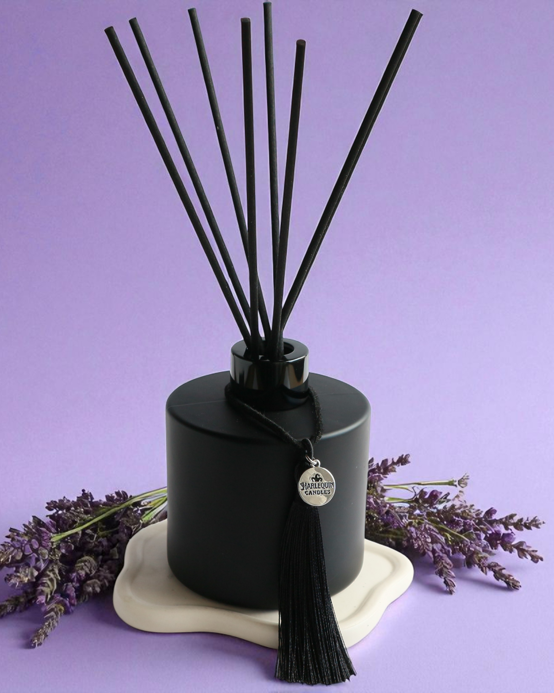 An Australian made Harlequin Candles black matte reed diffuser with a calming and relaxing fragrance of lavender and vanilla, set against a purple background with lavender sprigs.