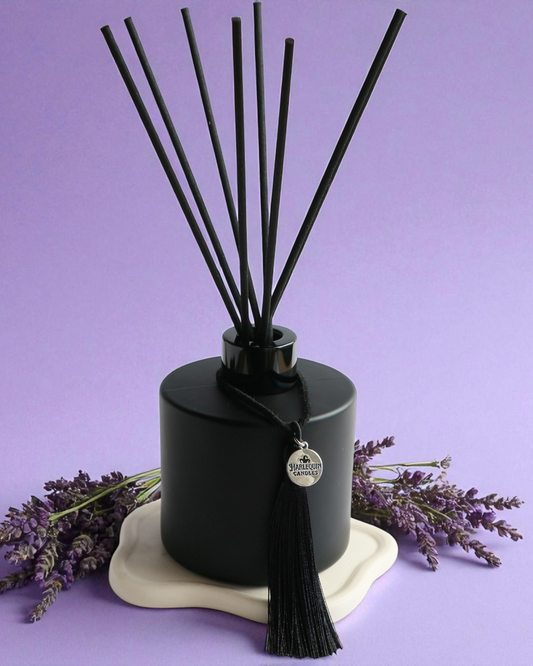 An Australian made Harlequin Candles black matte reed diffuser with a calming and relaxing fragrance of lavender and vanilla, set against a purple background with lavender sprigs.