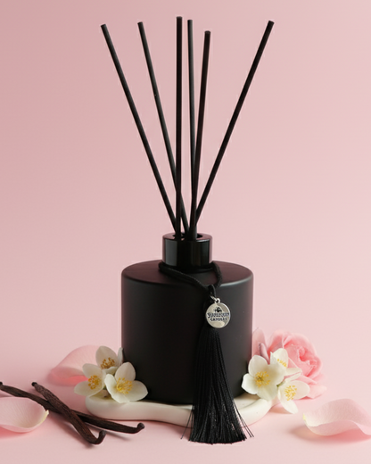 An Australian made Harlequin Candles black matte reed diffuser featuring a delicate floral home fragrance of marshmallow, musk, rose placed on a pink background.