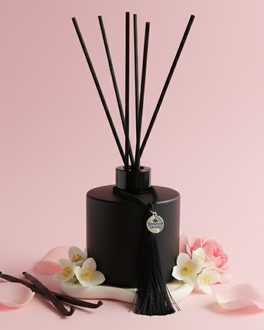 An Australian made Harlequin Candles black matte reed diffuser featuring a delicate floral home fragrance of marshmallow, musk, rose placed on a pink background.