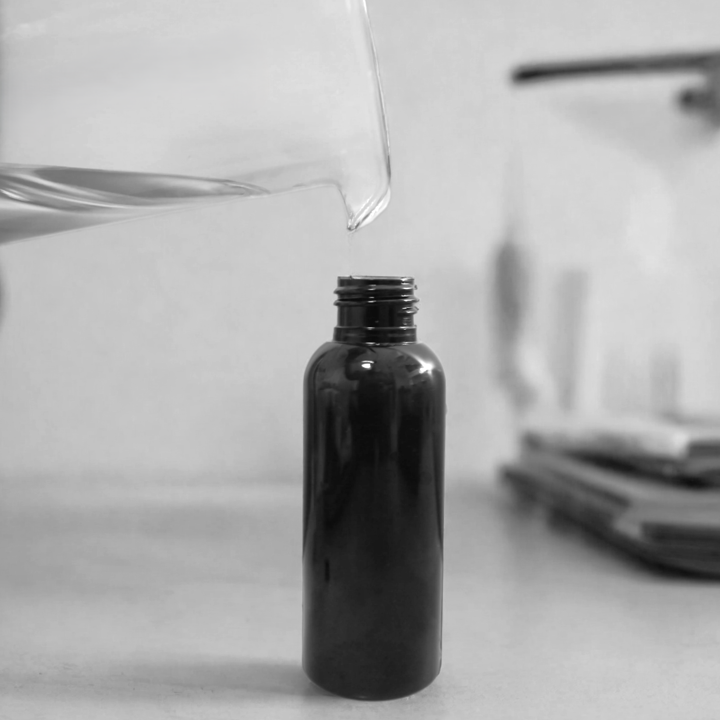 Behind the scenes at Harlequin Candles: Close-up of liquid being carefully poured from a beaker into a small brown bottle with a black pump, illustrating the craftsmanship of making our signature room mists.