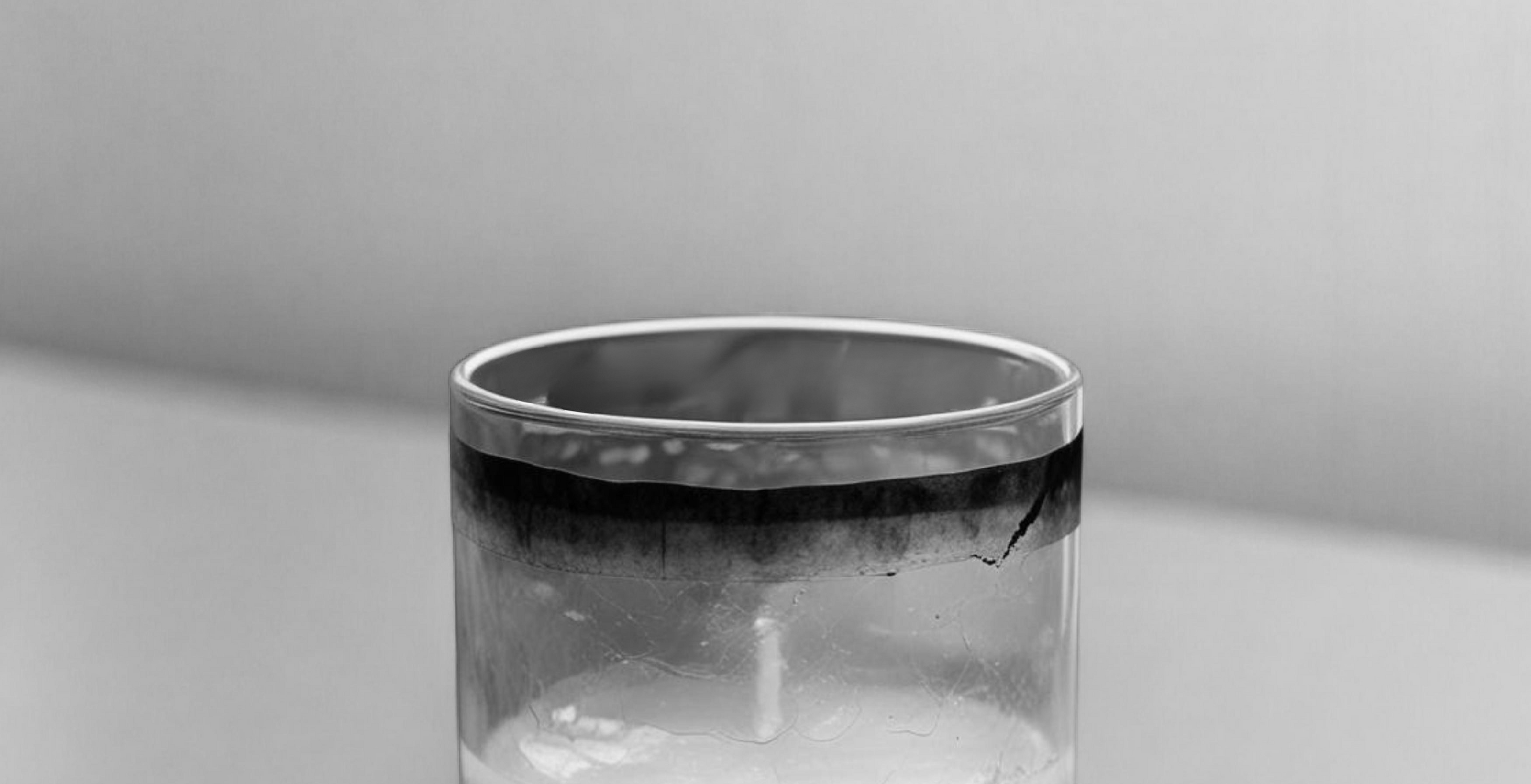 Close-up of a used candle in a clear glass jar showing a visible black ring of soot accumulated around the upper rim, illustrating the common issue of candle soot buildup and the need for proper wick trimming for clean burning.