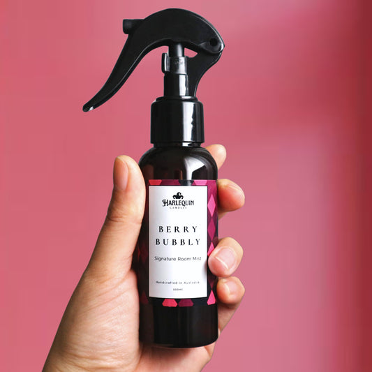 A Harlequin Candles Berry Bubbly Signature Room Mist in an amber spray bottle with a black trigger cap, placed against a two-toned background of light pink and white. The label clearly shows 'Harlequin Candles', 'Berry Bubbly', 'Signature Room Mist', and 'Handcrafted in Australia', highlighting this vibrant Australian-made home spray.