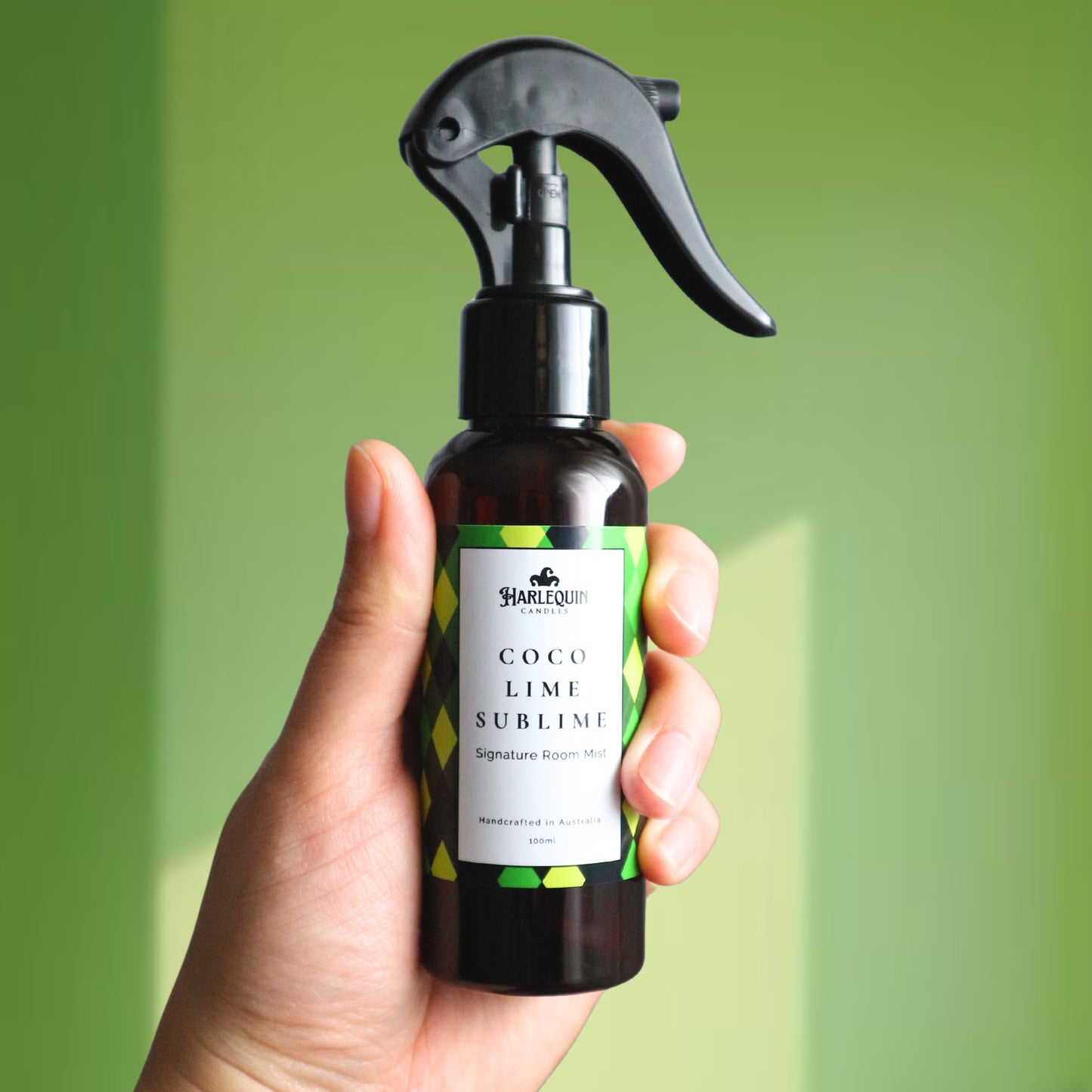 A Harlequin Candles Coco Lime Sublime Signature Room Mist in an amber spray bottle with a black trigger cap, placed against a two-toned background of light green and white. The label clearly shows 'Harlequin Candles', 'Coco Lime Sublime', 'Signature Room Mist', and 'Handcrafted in Australia', highlighting this tropical Australian-made home spray.