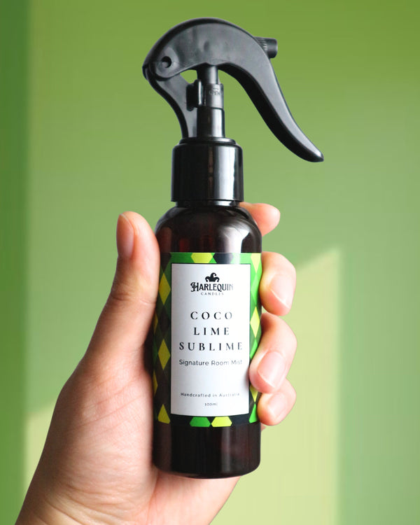 A Harlequin Candles Coco Lime Sublime Signature Room Mist in an amber spray bottle with a black trigger cap, placed against a two-toned background of light green and white. The label clearly shows 'Harlequin Candles', 'Coco Lime Sublime', 'Signature Room Mist', and 'Handcrafted in Australia', highlighting this tropical Australian-made home spray.