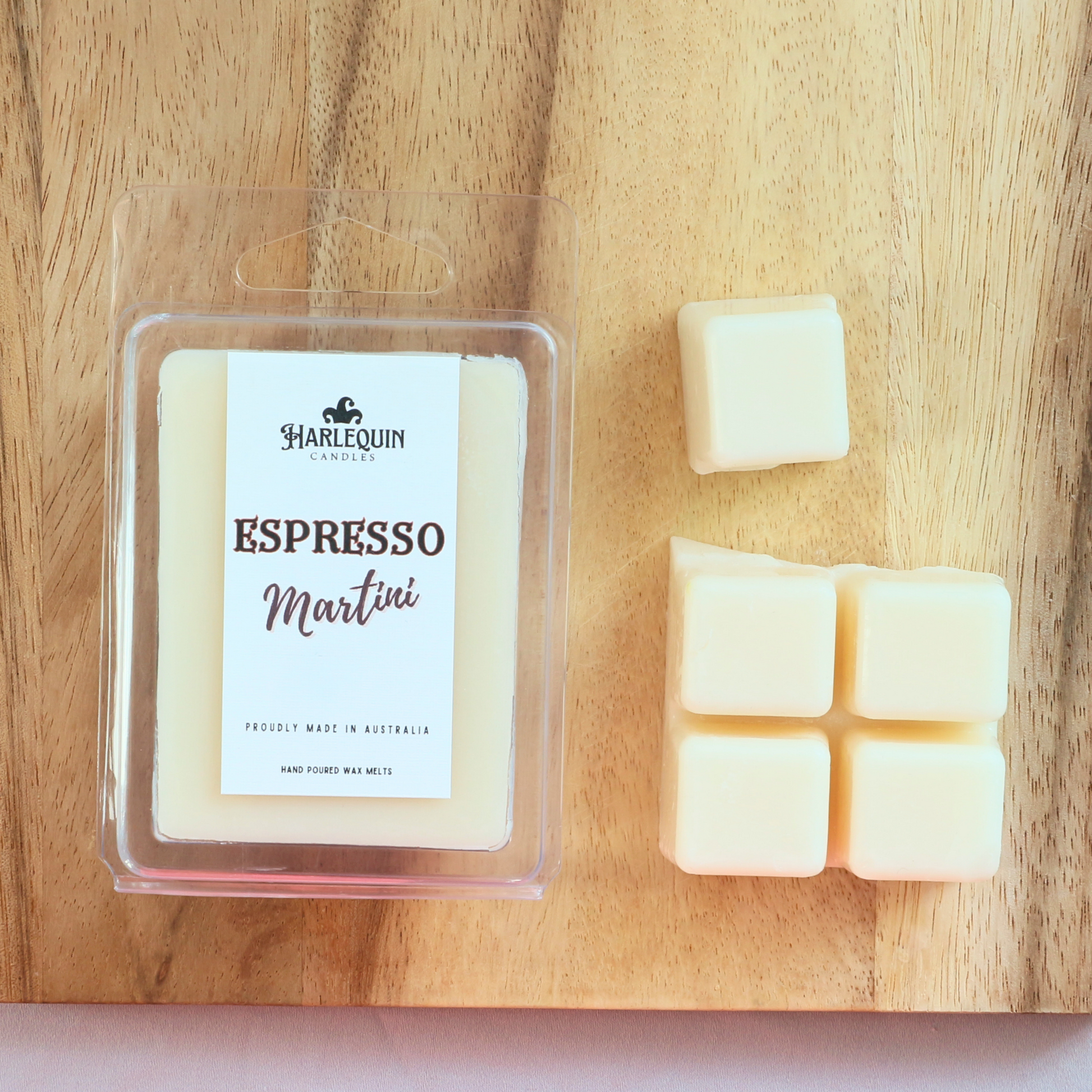 Harlequin Candles Espresso Martini soy wax melts, displayed in clear plastic clamshell packaging with the brand label. The label reads 'ESPRESSO Martini' and 'PROUDLY MADE IN AUSTRALIA HAND POURED WAX MELTS'. Several individual wax melt cubes are scattered on a light wooden cutting board, showcasing the coffee-scented home fragrance product and its local origin.