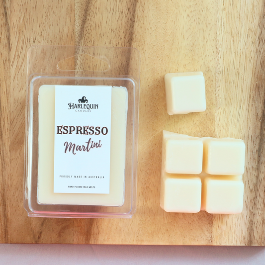 Harlequin Candles Espresso Martini soy wax melts, displayed in clear plastic clamshell packaging with the brand label. The label reads 'ESPRESSO Martini' and 'PROUDLY MADE IN AUSTRALIA HAND POURED WAX MELTS'. Several individual wax melt cubes are scattered on a light wooden cutting board, showcasing the coffee-scented home fragrance product and its local origin.