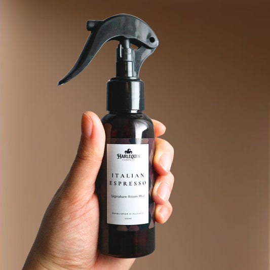 A Harlequin Candles Italian Espresso Signature Room Mist in an amber spray bottle with a black trigger cap, placed against a two-toned background of light pink and white. The label clearly shows 'Harlequin Candles', 'Italian Espresso', 'Signature Room Mist', and 'Handcrafted in Australia', highlighting this invigorating Australian-made home spray.
