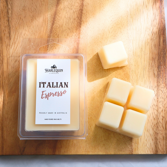 Harlequin Candles Italian Espresso soy wax melts, displayed in clear plastic clamshell packaging with the brand label. The label reads 'ITALIAN Espresso' and 'PROUDLY MADE IN AUSTRALIA HAND POURED WAX MELTS'. Several individual wax melt cubes are scattered on a light wooden cutting board, showcasing the coffee-scented home fragrance product and its local origin.