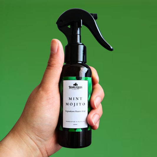 A Harlequin Candles Mint Mojito Signature Room Mist in an amber spray bottle with a black trigger cap, placed against a two-toned background of light green and white. The label clearly shows 'Harlequin Candles', 'Mint Mojito', 'Signature Room Mist', and 'Handcrafted in Australia', highlighting this refreshing Australian-made home spray.