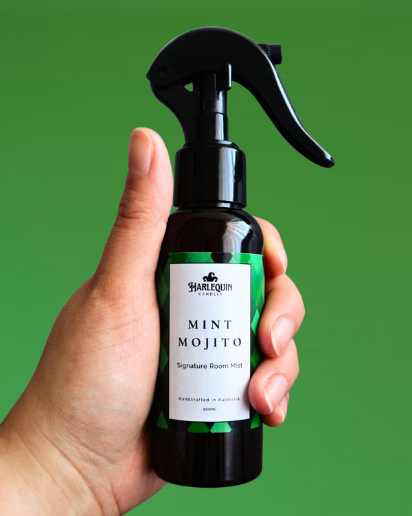 A Harlequin Candles Mint Mojito Signature Room Mist in an amber spray bottle with a black trigger cap, placed against a two-toned background of light green and white. The label clearly shows 'Harlequin Candles', 'Mint Mojito', 'Signature Room Mist', and 'Handcrafted in Australia', highlighting this refreshing Australian-made home spray.