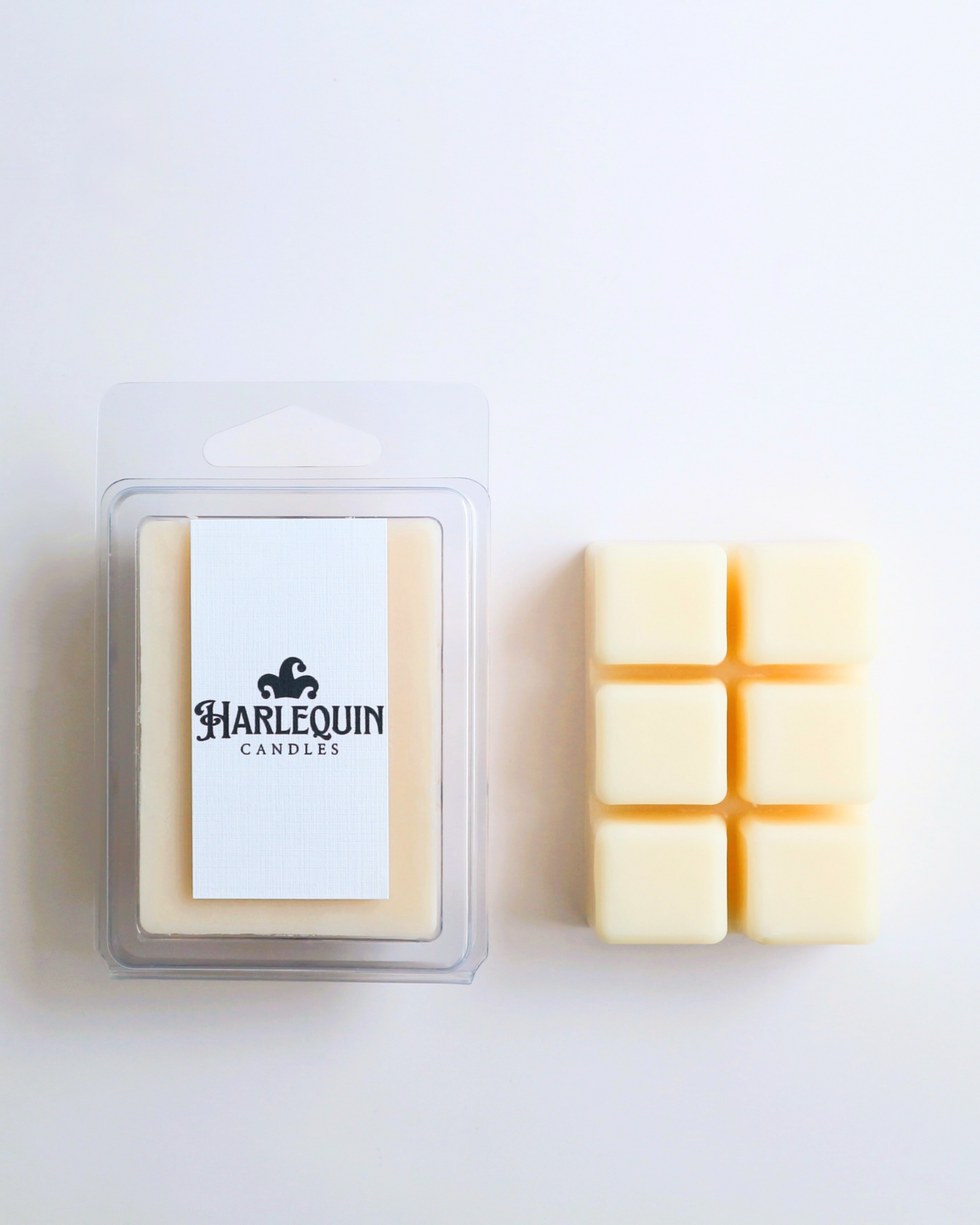 Harlequin Candles soy wax melts, featuring a clear plastic clamshell packaging with the brand label, displayed next to six individual wax melt cubes arranged on a light background. Showcases premium, eco-friendly home fragrance melts.