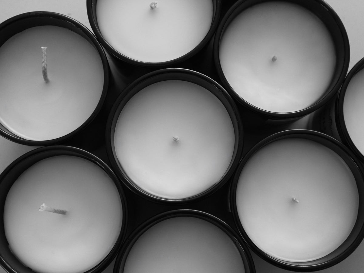 Overhead monochrome view of multiple unlit Harlequin Candles in sleek black jars, showing their white wax and wicks. The circular arrangement creates a minimalist and elegant display of the soy candle collection.