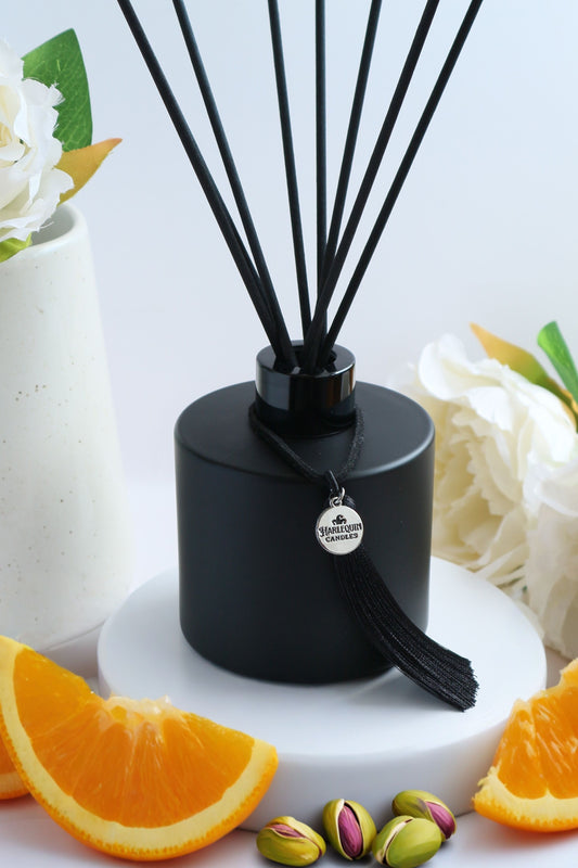 Harlequin Candles Tropical Tush reed diffuser in a matte black bottle with black reeds and a decorative black tassel. Scented like popular Brazilian bum creams, ideal for a summery home fragrance.