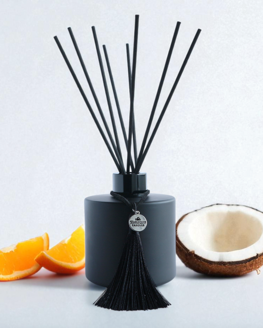 Harlequin Candles Tropical Tush reed diffuser in a matte black bottle with black reeds and a decorative black tassel. Scented like popular Brazilian bum bum creams, ideal for a summery home fragrance.