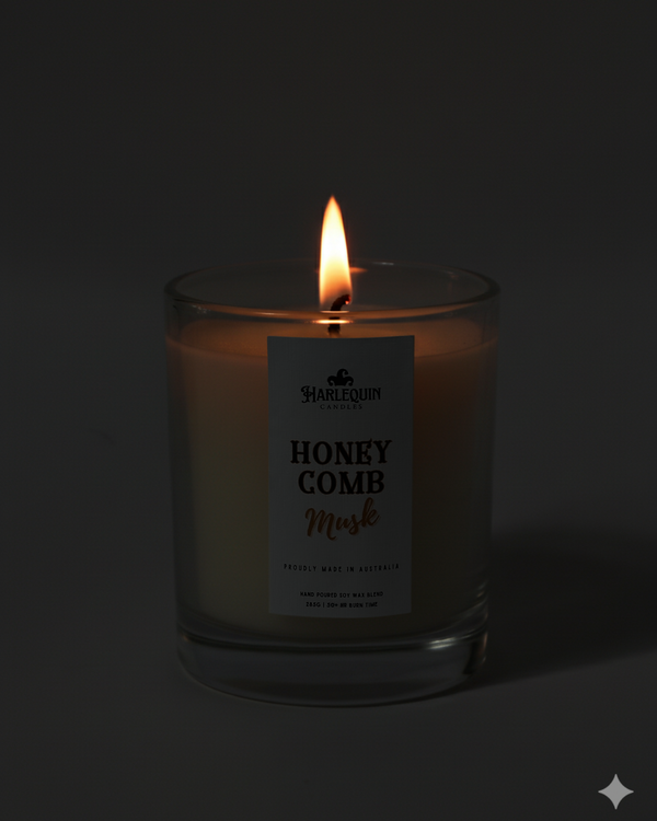 Lit Harlequin Candles Honeycomb Musk candle in a dark glass jar against a dark background, emphasizing the warm, cozy glow of the flame. Describes a proudly Australian-made, hand-poured soy wax candle.
