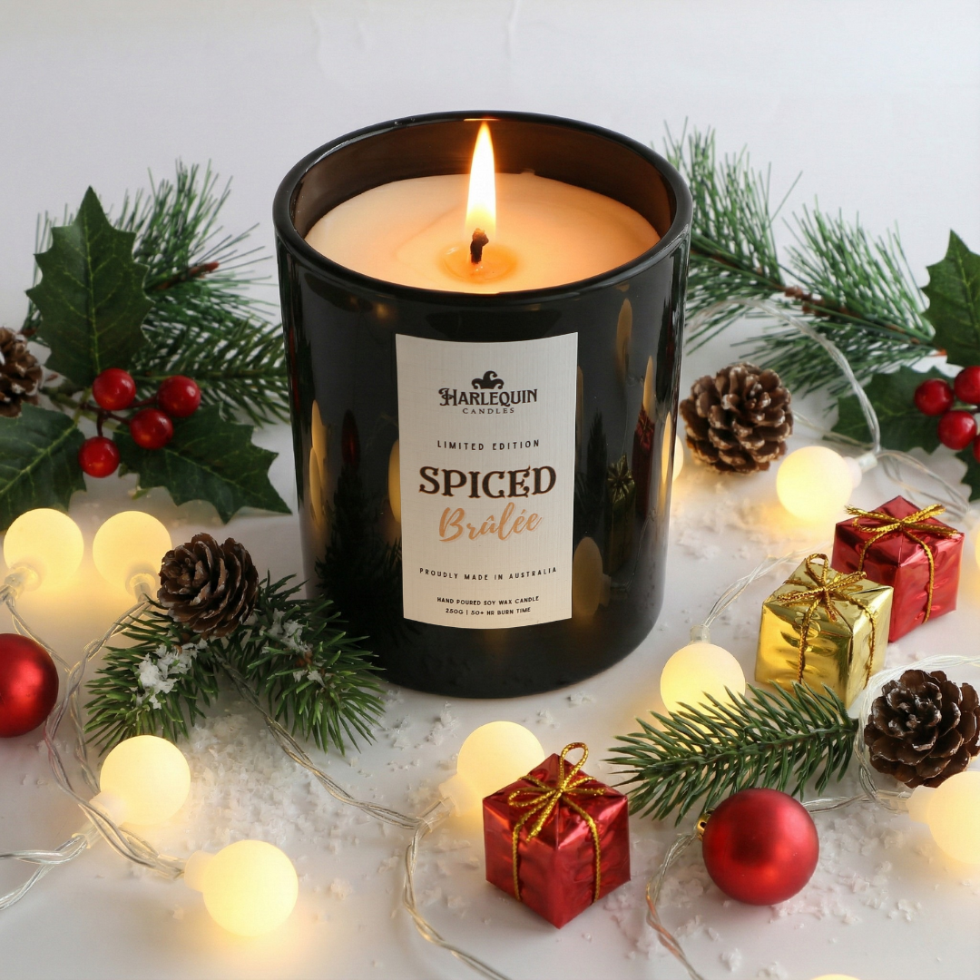 Harlequin Candles handpoured Spiced Brulee candle surrounded by Christmas decorations on a white surface. Limited Edition best for christmas gifting or treat for yourself.