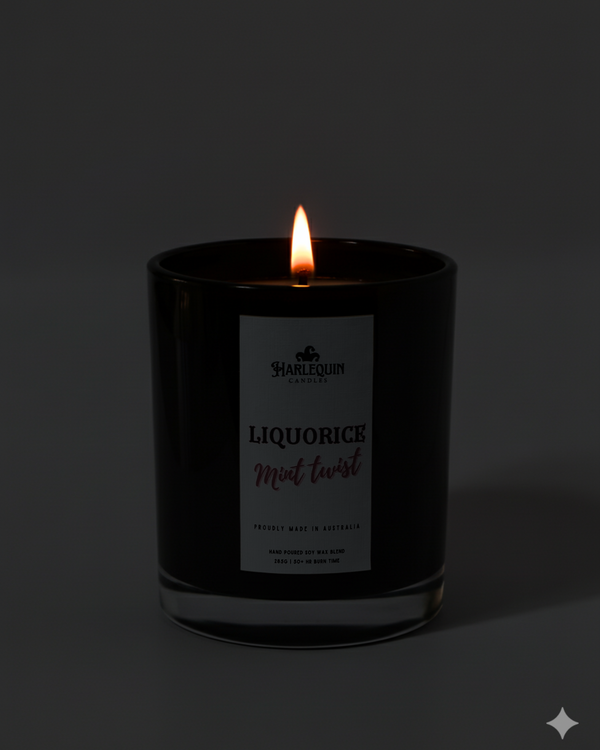 Lit Harlequin Candles Liquorice Mint Twist candle in a dark glass jar against a dark background, emphasizing the warm, cozy glow of the flame. Describes a proudly Australian-made, hand-poured soy wax candle.