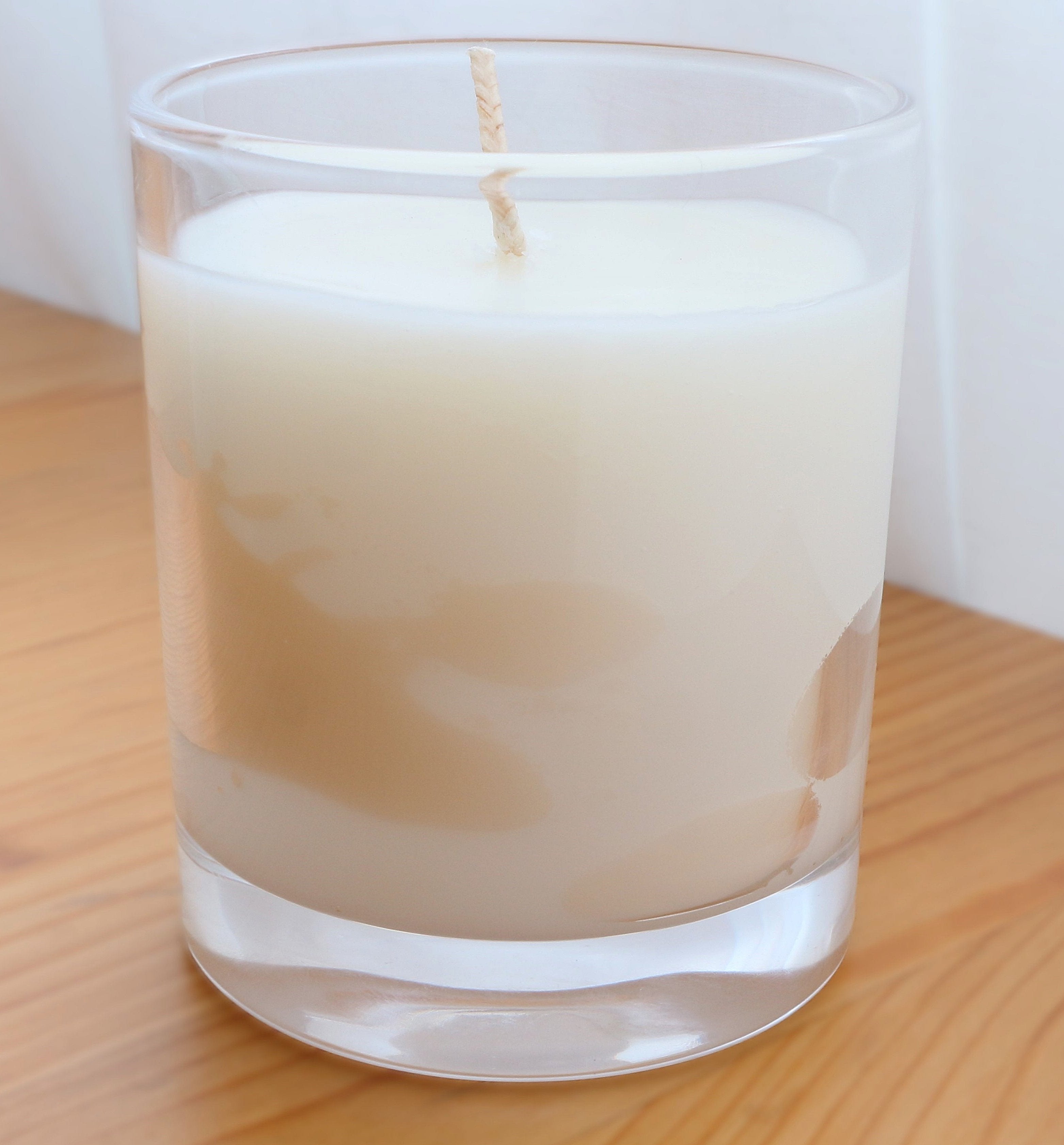 Close-up of an unlit soy wax candle in a clear glass jar, showing areas where the wax has pulled away from the glass, known as 'wet spots' or 'wax adhesion issues'. This is a natural characteristic of soy wax, indicating its purity.