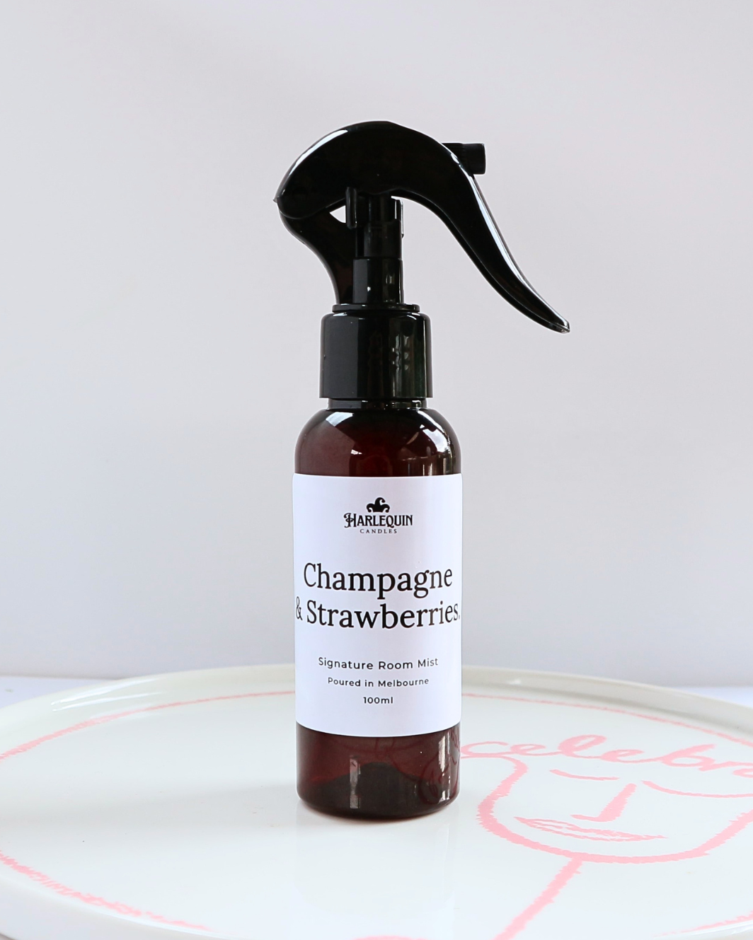 100ml amber bottle of Champagne and Strawberries signature room mist by Harlequin Candles, featuring a black trigger spray and minimalist white label.
