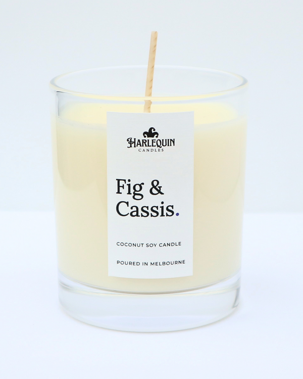 A close-up of a Harlequin Candles Fig & Cassis coconut soy candle in a clear glass jar. The minimalist white label features bold black typography and the text "Poured in Melbourne" against a bright, clean background.
