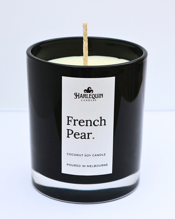 A close-up of a French Pear coconut soy candle by Harlequin Candles in a sleek, glossy black glass jar. The minimalist white label features the brand's logo and the text "Poured in Melbourne" against a clean, bright white background.