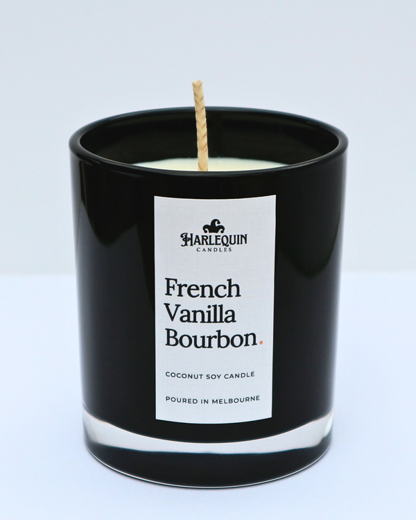 A close-up of a French Vanilla Bourbon coconut soy candle by Harlequin Candles in a sleek black glass jar. The minimalist white label features the brand's logo and the text "Poured in Melbourne" against a clean white background.