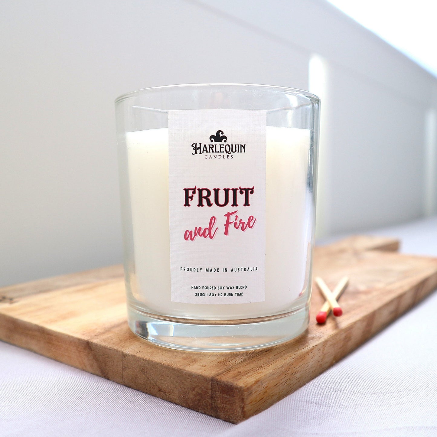 A "Fruit and Fire' Candle with white soy wax in a clean clear glass sitting on a wooden board. 