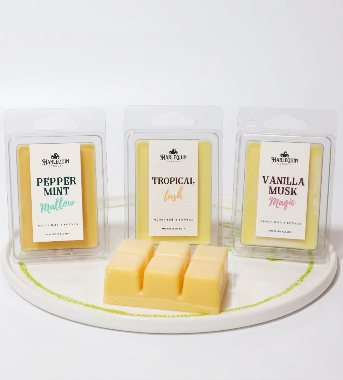 Three clamshell packages of handmade soy wax melts on a plate: Peppermint Mallow, Tropical Tush, and Vanilla Musk Magic. 100% soy wax, strong fragrance home scents.