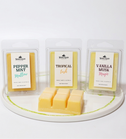 Three clamshell packages of handmade soy wax melts on a plate: Peppermint Mallow, Tropical Tush, and Vanilla Musk Magic. 100% soy wax, strong fragrance home scents.