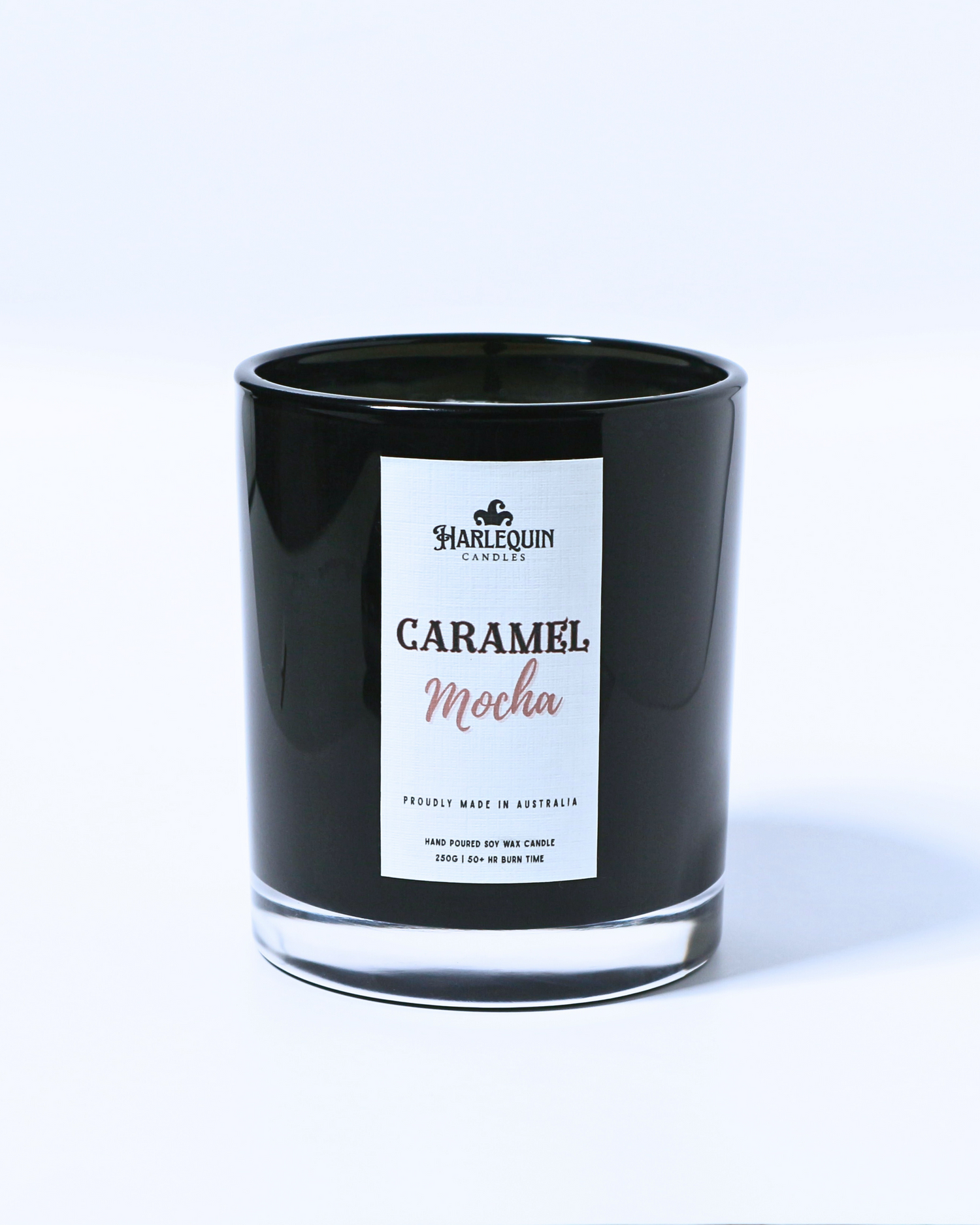 A Harlequin Candles "Caramel Mocha" hand-poured soy wax candle in a black glass jar, resting on a blue book. Premium Australian made scented candle.