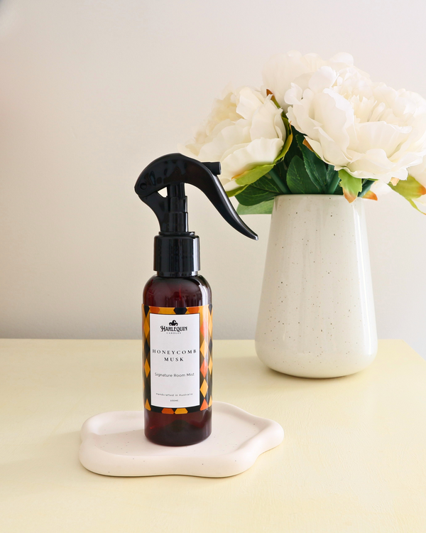 Handcrafted Australian Honeycomb Musk room mist by Harlequin Candles, presented in a luxe amber spray bottle on a textured woven mat against a soft neutral background.